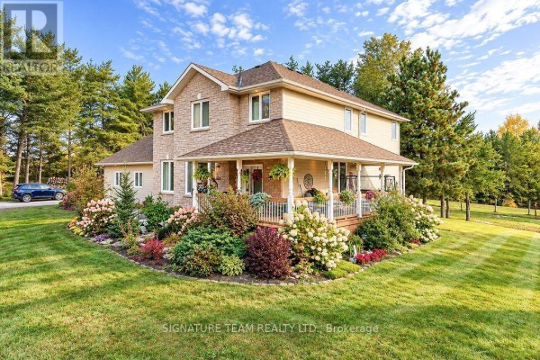Side view of a stone and tan house with a covered porch surrounded by blooming gardens. - 368 Dombroskie Road, Whitewater Region