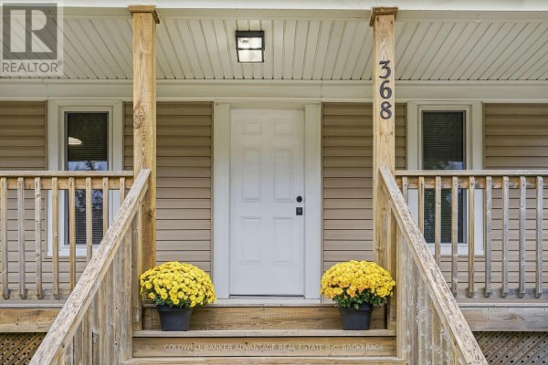 Close-up of the white front door and porch railing, with yellow mums flanking the stairs. - 368 Niagara Street, Welland