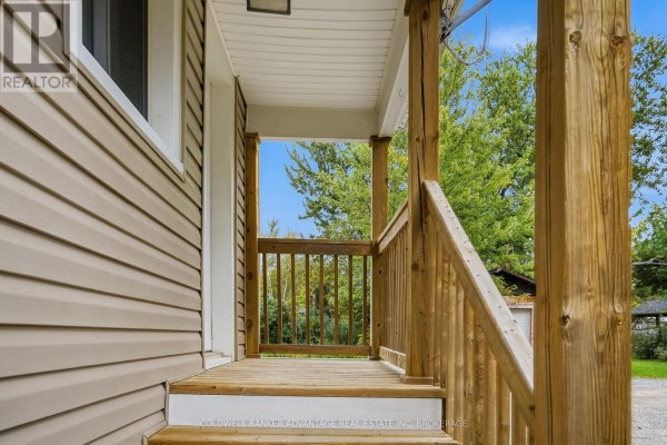 View from the porch looking out towards the backyard, showing wooden railings and trees. - 368 Niagara Street, Welland