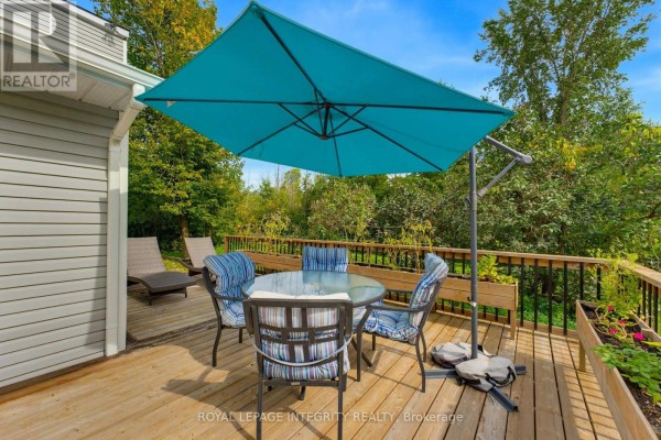 Outdoor dining set with a large blue umbrella on a wooden deck overlooking a wooded area. - 368 Ramsay Concession 5a Road, Mississippi Mills