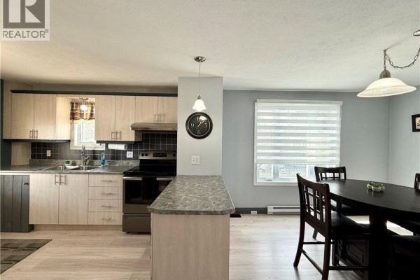 Open kitchen and dining area with wooden table, gray countertops, and natural light - 3688 Principale Street, Baker Brook