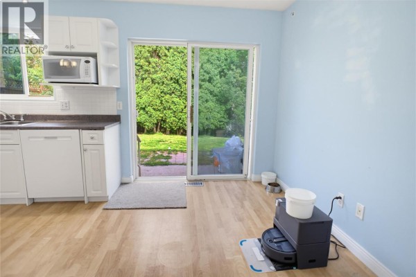 Kitchen area with light blue walls, a sliding glass door leading to a backyard, and laminate flooring. - 369 Coyote Drive, Kamloops