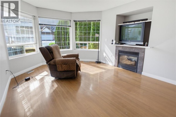 Living room with a bay window, a gas fireplace with a tile surround, and light wood laminate flooring. - 369 Coyote Drive, Kamloops