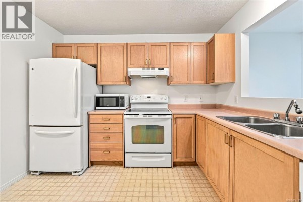 U-shaped kitchen with light wood cabinets, white appliances, and a beige tiled floor. - 369 Petroglyph Cres, Nanaimo
