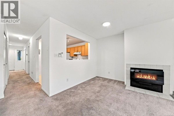 Living room with grey carpet, white walls, and a modern black fireplace with a white tile surround. - 369 Petroglyph Cres, Nanaimo