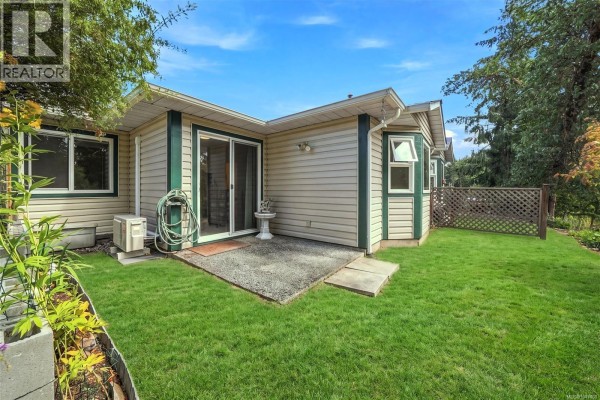 Backyard patio area with green grass, mature trees, and a sliding glass door. - 369 Petroglyph Cres, Nanaimo