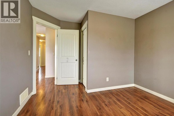 Bedroom with wood-look laminate flooring and a doorway opening to a hallway. - 369 Wallace Road, Kelowna