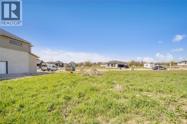 Cleared land with green grass, utility markers, and new home construction visible in the distance. - 3697 Farrow Avenue, Windsor