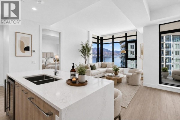 Modern kitchen island with waterfall countertop opens to living room with sectional sofa and large windows. - 3699 Capozzi Road Unit# Ph6, Kelowna
