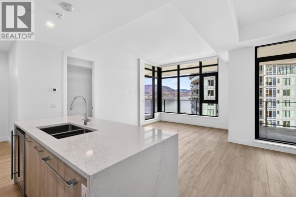 Modern kitchen island with sink opens to living area with large windows and a city view. - 3699 Capozzi Road Unit# Ph6, Kelowna