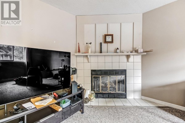 Living room with a white tiled fireplace, a black metal screen, and a dark wood entertainment unit with a television. - 37 - 455 Springbank Avenue N, Woodstock