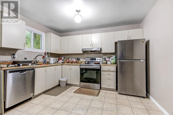 Kitchen with cream-colored cabinets, stainless steel appliances including a refrigerator and dishwasher, and beige tiled flooring. - 37 - 455 Springbank Avenue N, Woodstock