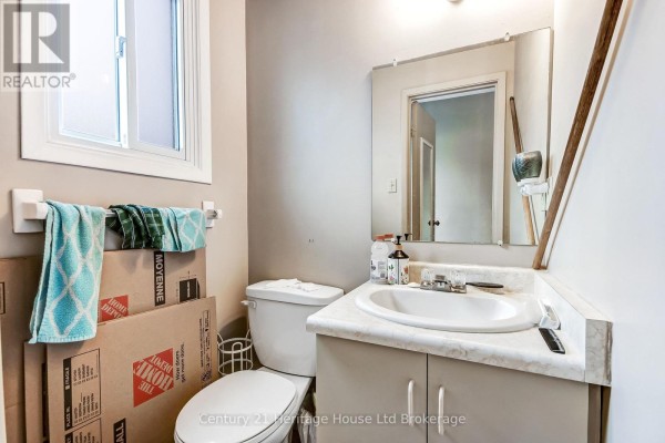 Small bathroom with a white vanity, toilet, and mirror, featuring stacked moving boxes in the corner. - 37 - 455 Springbank Avenue N, Woodstock