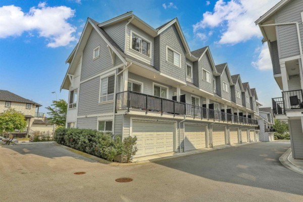 Side view of a grey townhouse complex with garages and balconies under a blue sky. - 37 12830 62 Avenue, Surrey