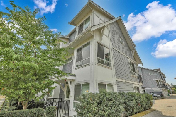 Corner view of a grey townhouse with white trim and dark windows, bordered by trees. - 37 12830 62 Avenue, Surrey
