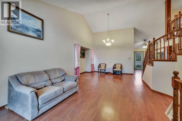 Living room with vaulted ceiling, wood floors, and beige sofa. - 37 Denovan Crescent, Red Deer