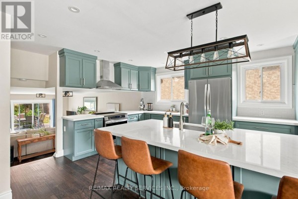 Open concept kitchen and living space with teal cabinets, island, dark wood floor, and view to backyard. - 37 Maple Avenue W, New Tecumseth