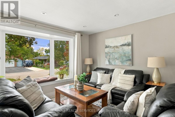 Living room with black leather sofas, a wooden coffee table, and a large bay window overlooking the street. - 37 Maple Avenue W, New Tecumseth