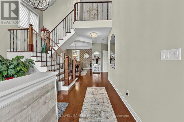 Spacious foyer with dark wood floors, a sweeping staircase with black railing, and arched doorways. - 37 Mcgovern Street, New Tecumseth