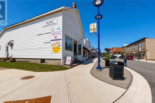 Side view of the white commercial building with signage, showing the street and adjacent stone building. - 37 Meredith Street, Gore Bay