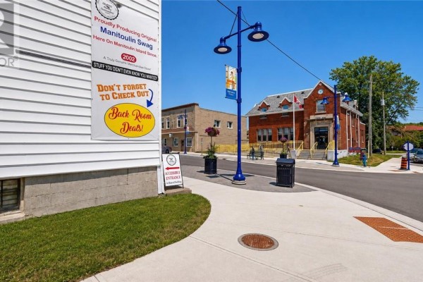 Close-up of signs on the white commercial building with a view of the street and brick post office. - 37 Meredith Street, Gore Bay