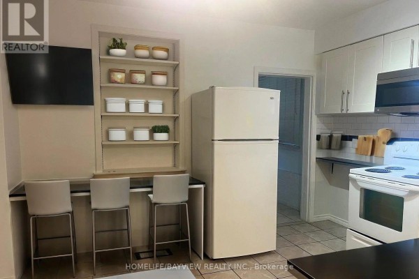 Kitchen area with built-in shelving, three bar stools at a counter, and a refrigerator. - 37 Sellers (main Floor) Avenue, Toronto