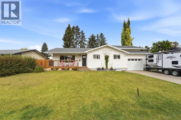 Front exterior of a white bungalow with a well-maintained lawn and trees, a travel trailer is parked in the driveway. - 37 Sherwood Crescent, Red Deer