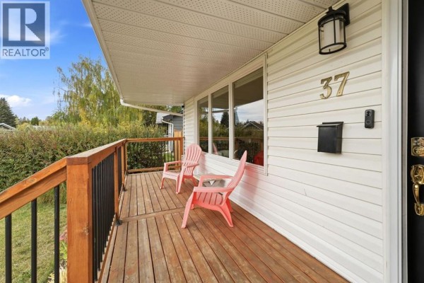Close-up of a wooden deck with black railings, two pink chairs, and the front of the house with siding and address number. - 37 Sherwood Crescent, Red Deer