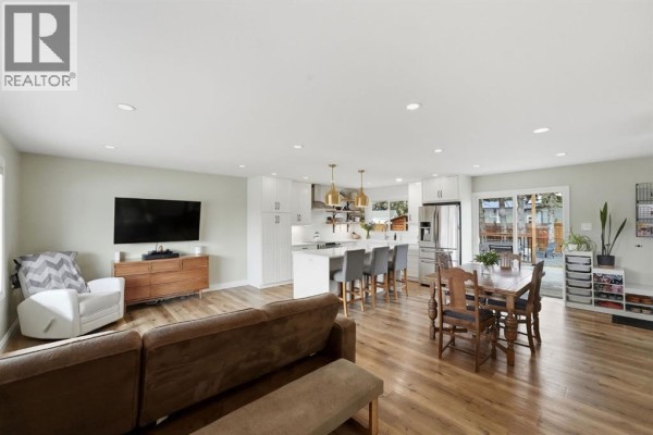 Open-concept living, dining, and kitchen area with light wood floors, modern white cabinetry, and island seating. - 37 Sherwood Crescent, Red Deer