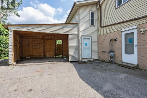 Carport attached to the side of a house with a concrete floor and open wooden structure. - 37 Tinbury Place, Toronto