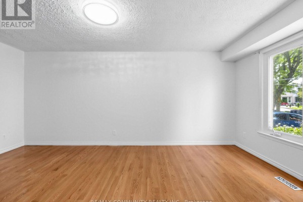 Empty living room with white walls, hardwood floors, and a large window overlooking the street. - 37 Tinbury Place, Toronto