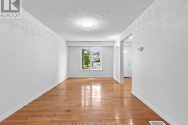 Empty dining room with white walls, hardwood floors, and a window showing the street outside. - 37 Tinbury Place, Toronto