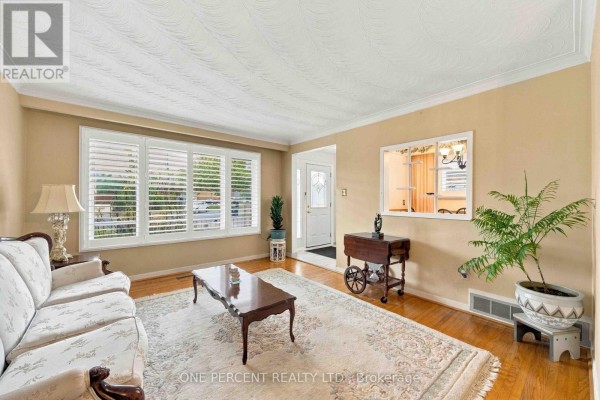 Living room with a sofa, coffee table, plantation shutters, and a view through to the foyer. - 37 Wilmont Drive, Toronto