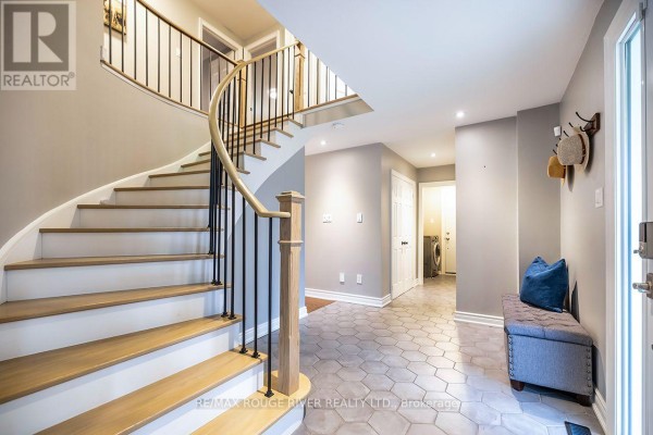 Interior foyer with a curved wooden staircase, black railing, and hexagonal floor tiles. - 37 Wyndfield Crescent, Whitby