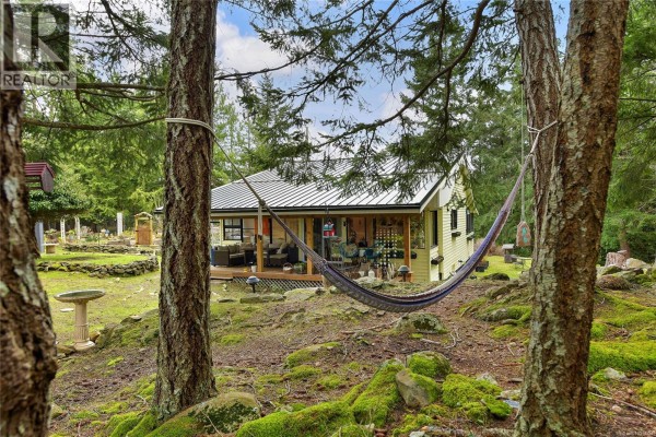 View of the house from between two trees, showcasing the outdoor seating area. - 370 Campbell Bay Rd, Mayne Island