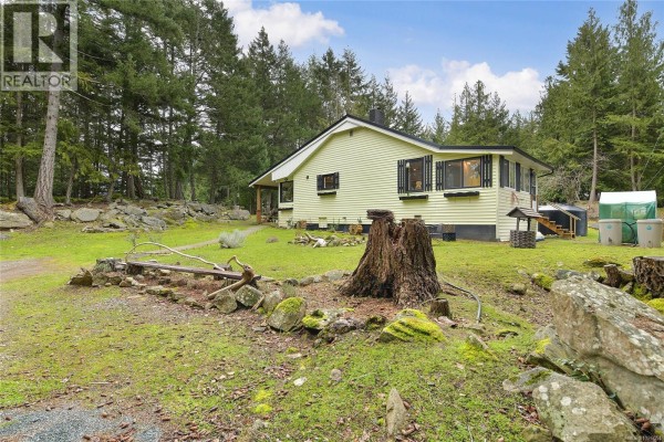 Backyard view of the house with a gravel path and surrounding trees. - 370 Campbell Bay Rd, Mayne Island