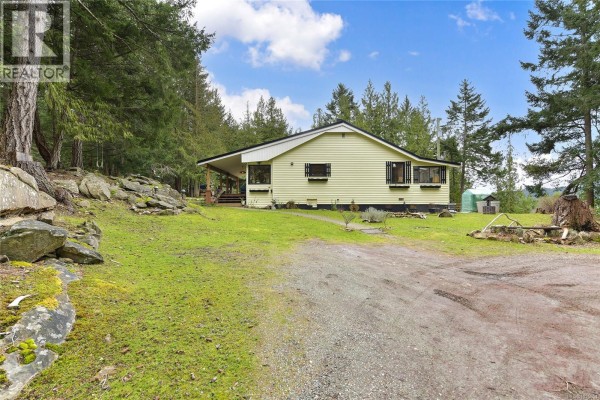 Driveway leading to the house, surrounded by greenery and rocky landscaping. - 370 Campbell Bay Rd, Mayne Island