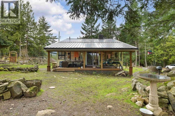 Rear view of the house with a deck, garden space, and stone features. - 370 Campbell Bay Road, Mayne Island