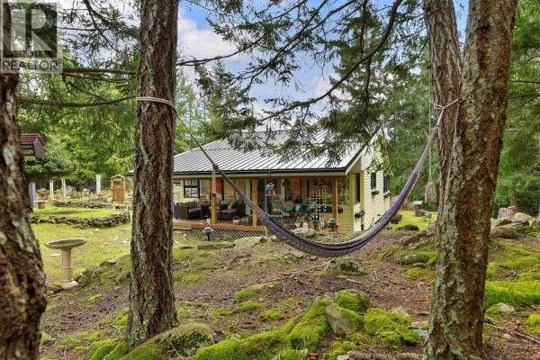 Hammock between trees with a view of the house and surrounding greenery. - 370 Campbell Bay Road, Mayne Island
