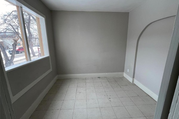 Room with tiled floor, gray walls, and a large window offering a street view. An arched doorway is on the right. - 370 Pritchard Avenue, Winnipeg