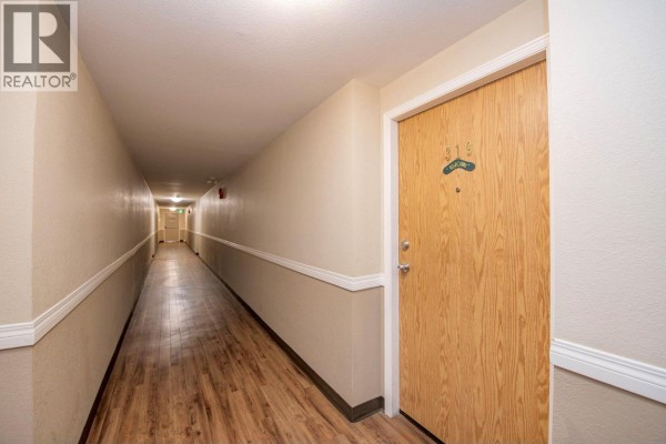 Long apartment hallway with wood-look flooring and beige walls leading to apartment 319. - 3700 28a Street Unit# 319, Vernon