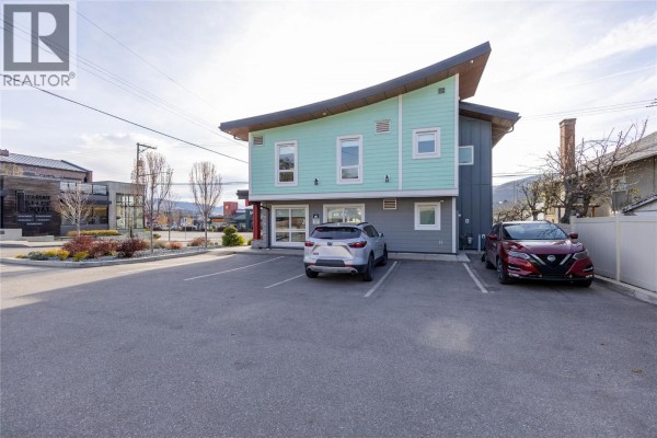 Side view of a light blue commercial building with a gray lower level, parking lot, and residential buildings in the background. - 3701 27 Street, Vernon