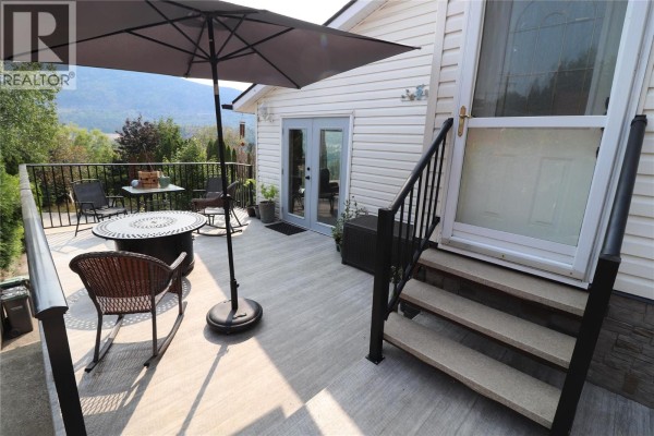 Second-floor deck with seating, umbrella, and stairs to the house. - 3702 9th Avenue, Castlegar