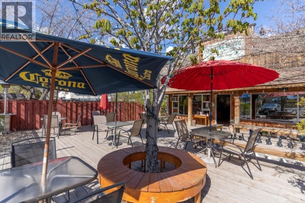Outdoor seating area with tables, chairs, and umbrellas on a wooden deck. - 3705 Riverview Avenue, Ashcroft