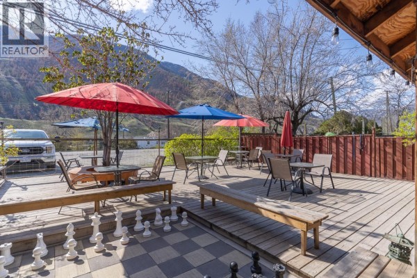 Deck seating area with umbrellas, tables, chairs, benches, and a giant chessboard. - 3705 Riverview Avenue, Ashcroft