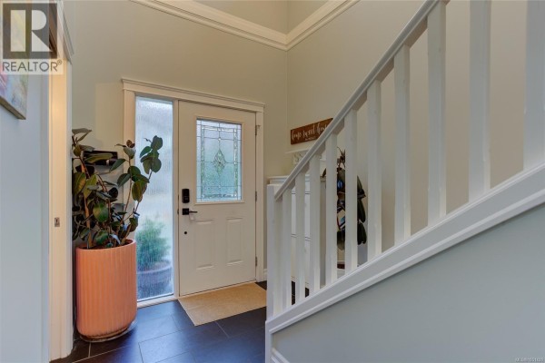 Interior view of a home entrance with a white door featuring frosted glass and a white staircase. - 3706 Cornus Crt, Langford