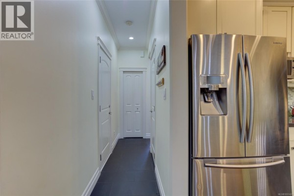 Interior hallway with dark tile flooring, white doors, and a stainless steel refrigerator on the right. - 3706 Cornus Crt, Langford