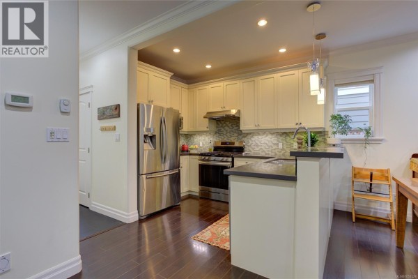 View of a kitchen with cream-colored cabinets, stainless steel appliances, dark countertops, and hardwood floors. - 3706 Cornus Crt, Langford