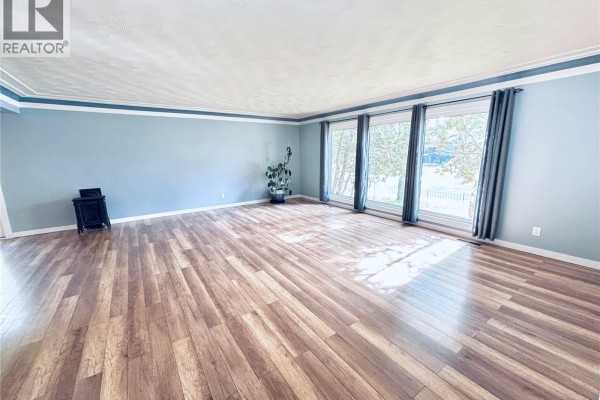 Empty living room with light blue walls, hardwood floors, and large windows with grey curtains. - 3708 Lakeview Avenue, Regina