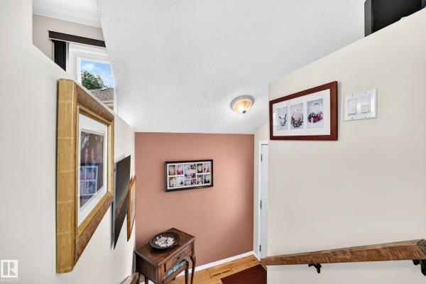 Interior hallway with a small wooden table, framed photos, and a staircase. - 371 Kirkpatrick Cr Nw, Edmonton